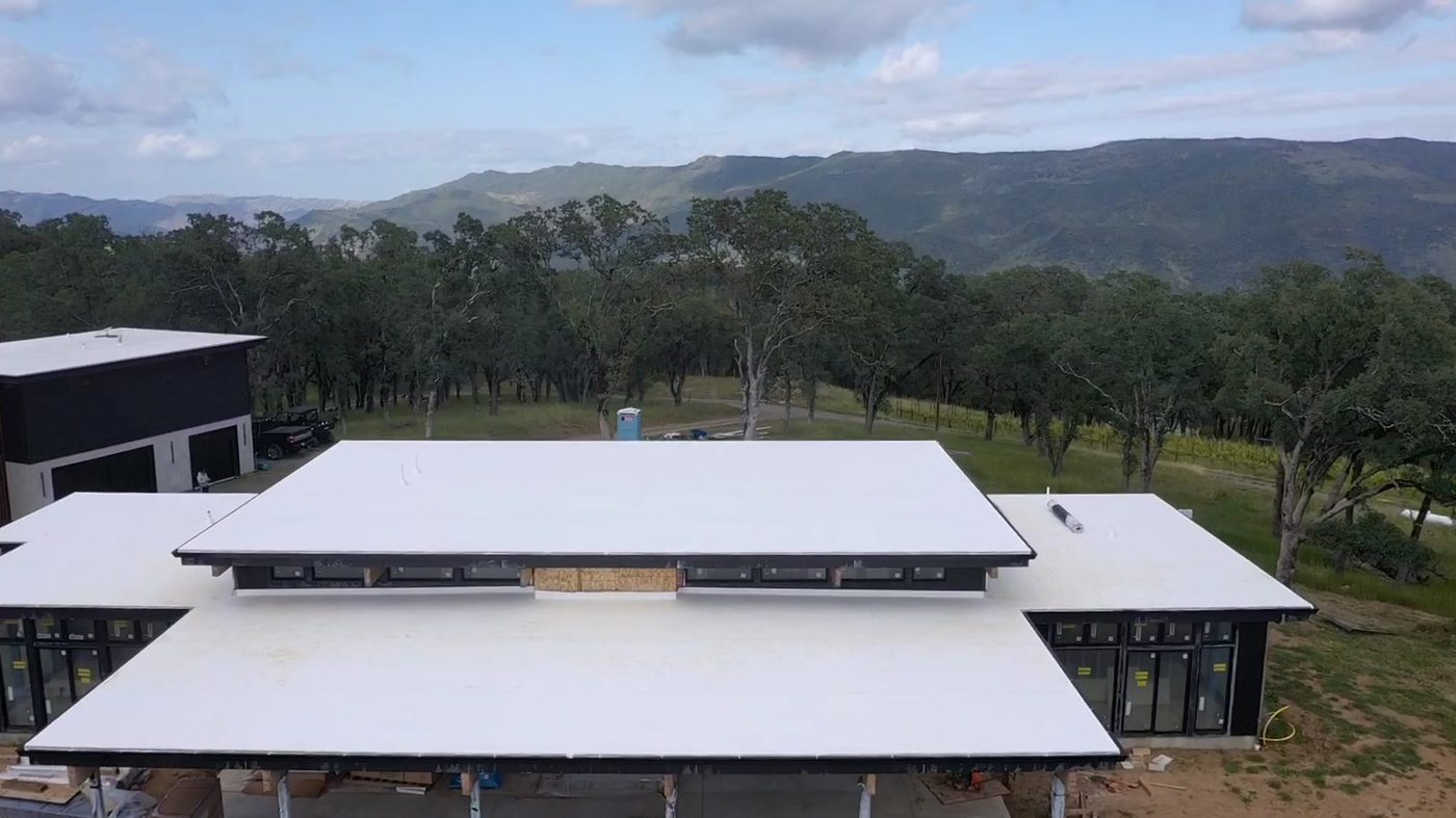 Rear elevation of the Napa Valley Lindal home under construction, showing vertical cedar detailing and standing-seam metal roof against oak woodland.